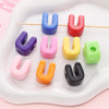 A collection of colorful acrylic letter beads shaped like the letter U arranged on a white tray.