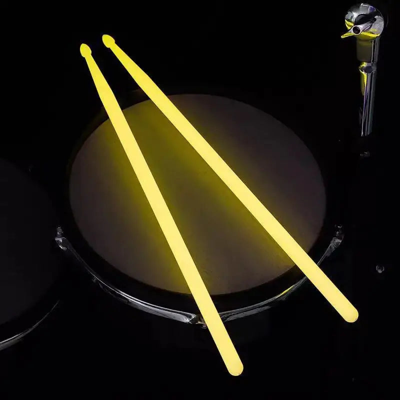 Pair of glow-in-the-dark nylon drumsticks casting a bright yellow light against a dark background.