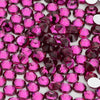 A close-up view of various pink and magenta glass crystal flatback rhinestones for nail art and crafts.