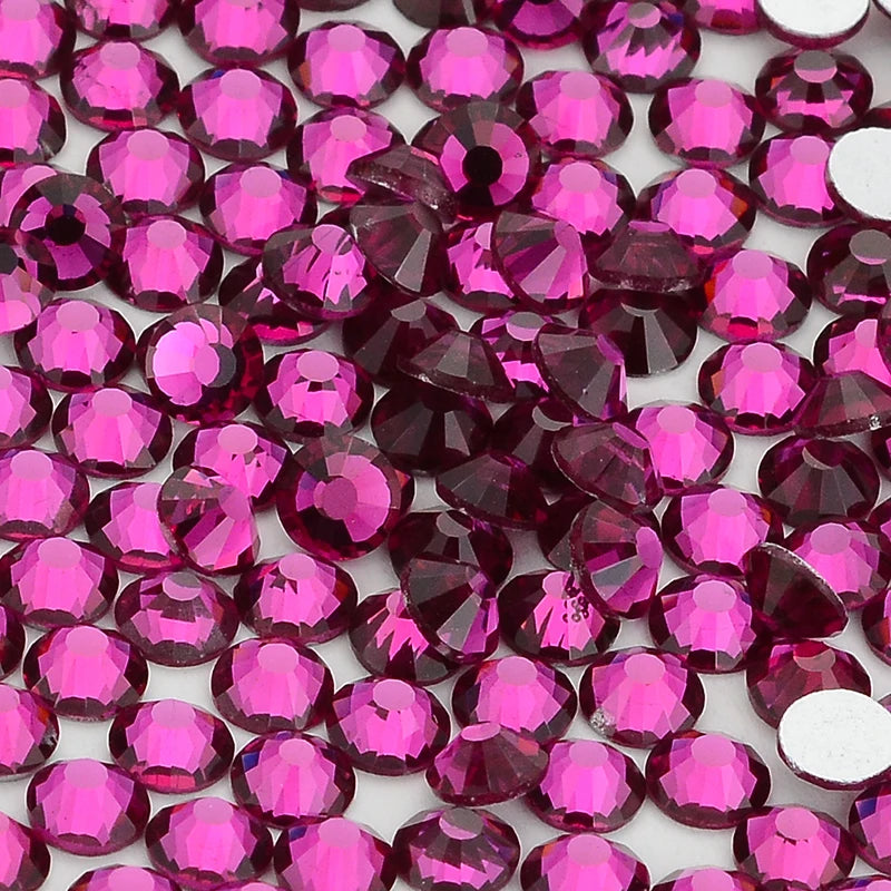 A close-up view of various pink and magenta glass crystal flatback rhinestones for nail art and crafts.