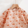 A light peach patterned baby bib with long sleeves displayed on a wooden hanger.