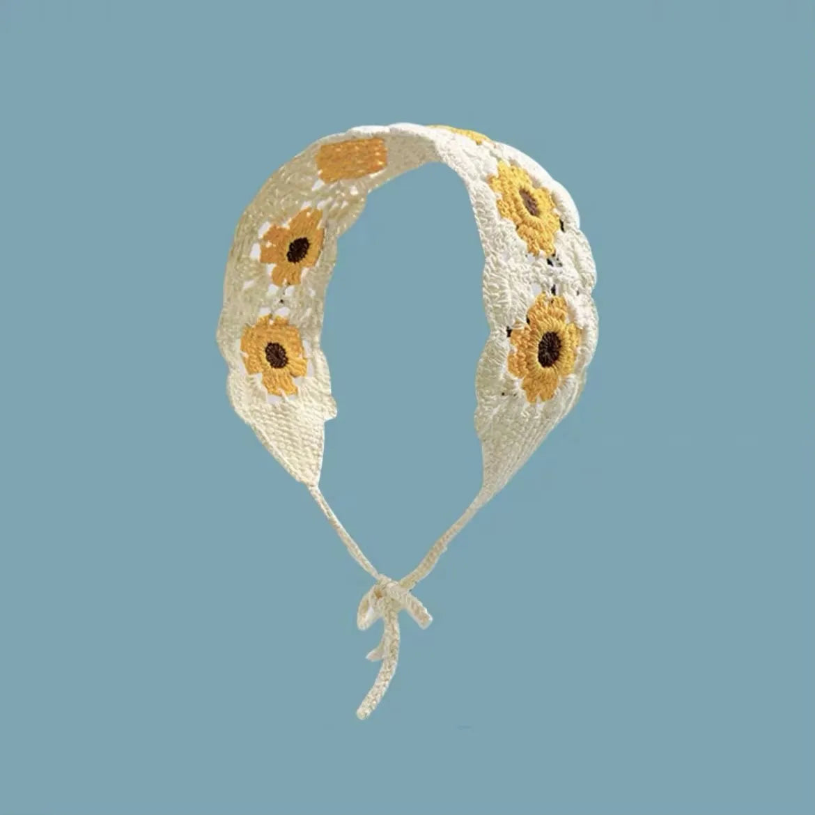 A handmade crochet headband featuring yellow and orange daisy patterns on a cream-colored fabric.
