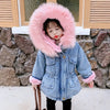 A young girl models a light blue denim jacket with a pink faux fur collar outdoors.