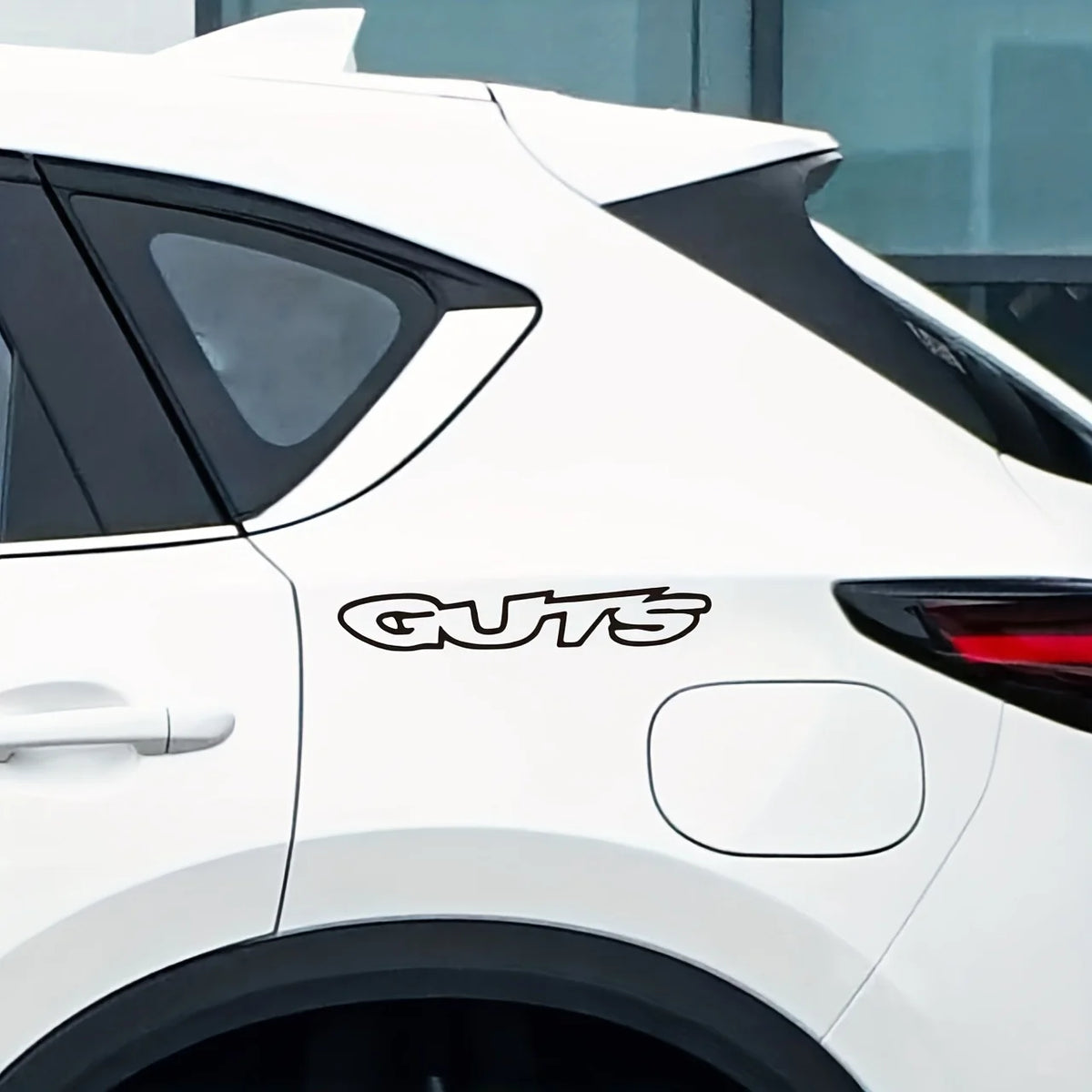 A white car with a black roof spoiler features the GUTS letter waterproof vinyl sticker on the side panel.
