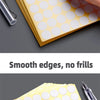 A close-up of round self-adhesive dot labels in yellow and white are shown being written on with a pen.