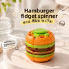 An orange and green burger-shaped fidget spinner toy resting on a white plate.