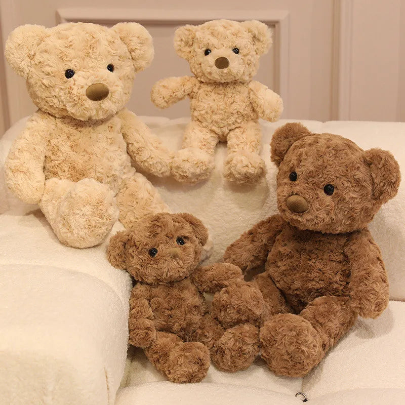 A collection of three soft brown teddy bear plush toys sitting on a white surface.