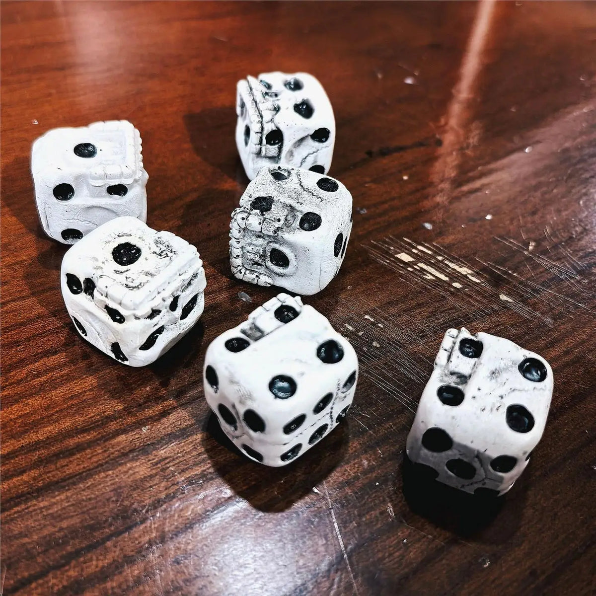 A set of five white skull dice resting on a dark wooden surface.
