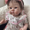 A lifelike 18-inch reborn baby doll with hand-painted details wearing a pink floral dress and bow.