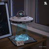 A clear dome model of an alien spaceship sits on a display base with glowing blue lights, next to building blocks.