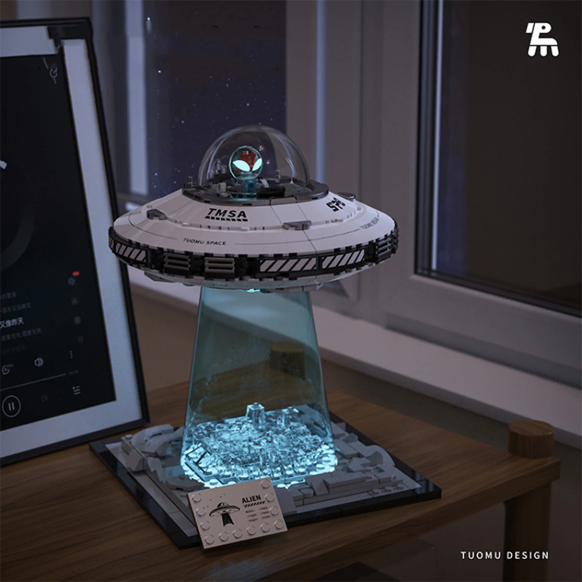 A clear dome model of an alien spaceship sits on a display base with glowing blue lights, next to building blocks.