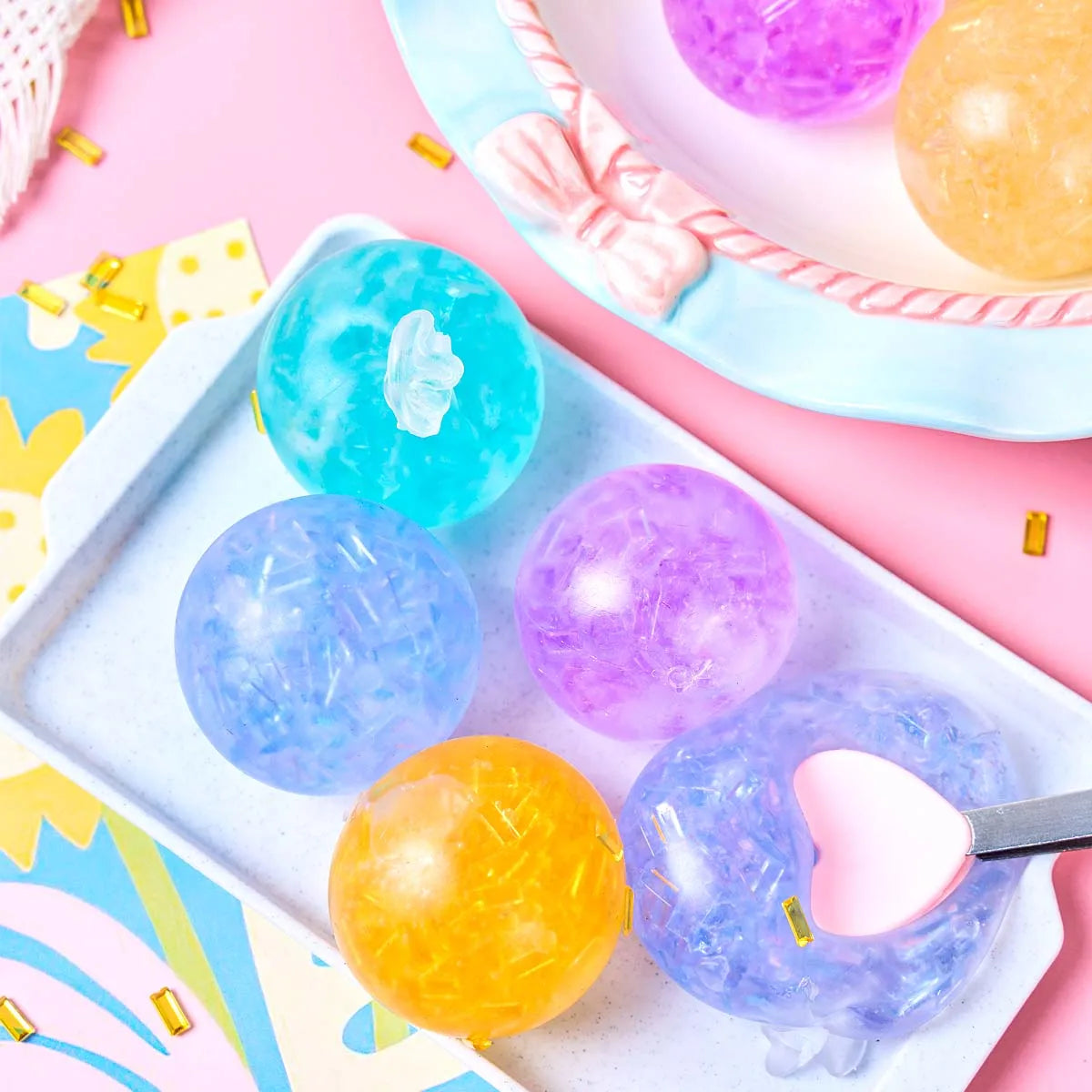A set of six colorful, translucent soft squeeze balls in shades of blue, purple, and yellow resting on a white tray.