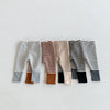 A row of baby leggings featuring various striped and solid color designs in gray, brown, beige, black, and white.