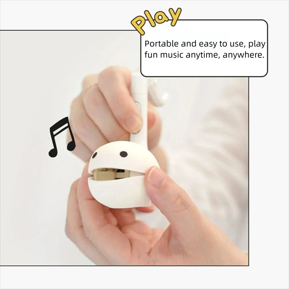 A hand holds a white electronic musical instrument toy, the Otamatone Mini, ready to play.