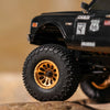 Black RC buggy with gold beadlock wheels and a large tire on a rock surface.