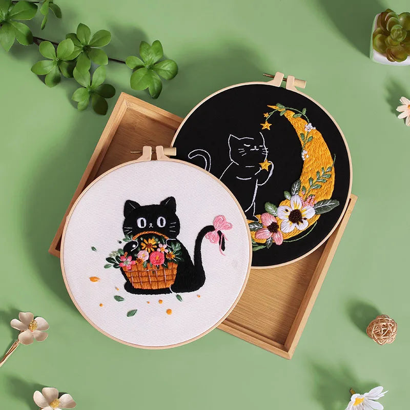 A set of embroidery tools and instructions for a moon and black cat design on canvas.
