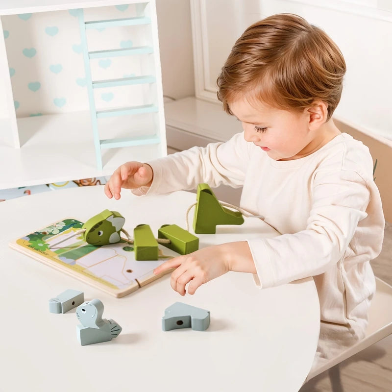 A toddler is playing with a wooden animal threading and stacking toy set on a white table.