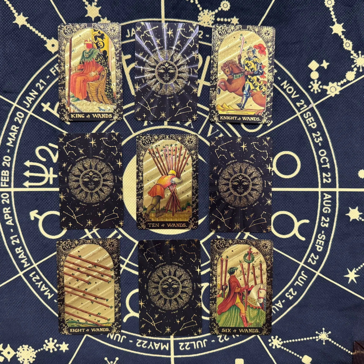 A collection of mini gold foil tarot cards arranged in a circular layout on a dark blue fabric background.