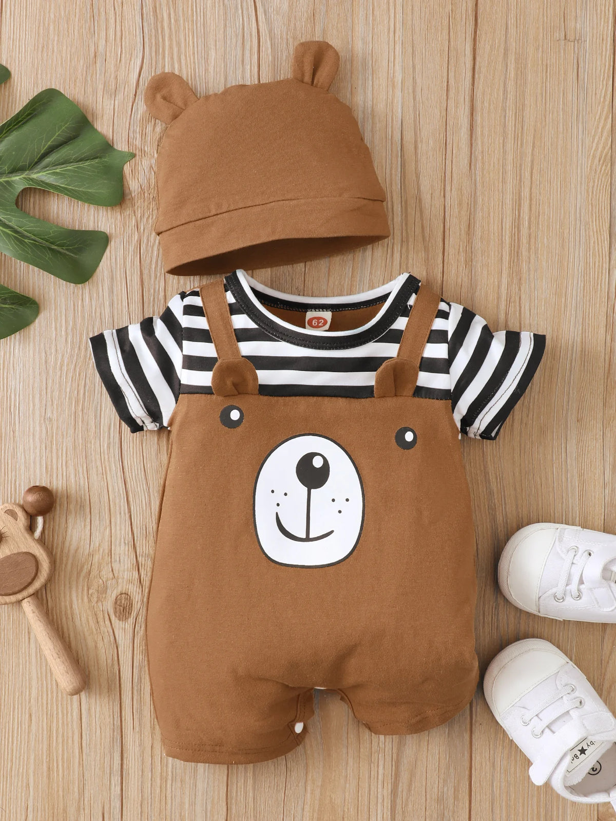 A brown baby bear print short sleeve romper and matching hat lying on a wooden surface.