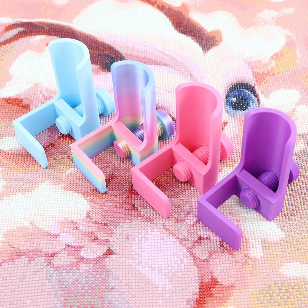 Four colorful adjustable diamond painting canvas stands with table clamps and rollers arranged on a pink background.