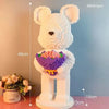 A white bear sculpture made of building blocks with pink and purple flowers, standing on a base.
