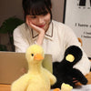 A yellow plush toy shaped like a duck is displayed on a wooden surface next to a person.