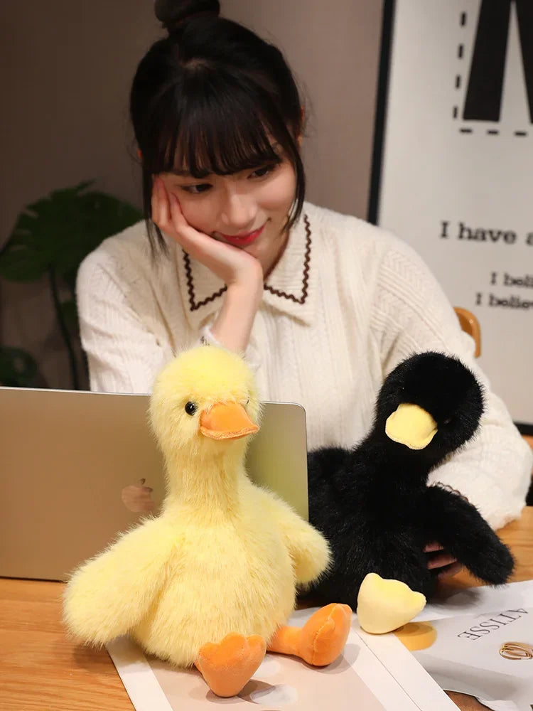 A yellow plush toy shaped like a duck is displayed on a wooden surface next to a person.