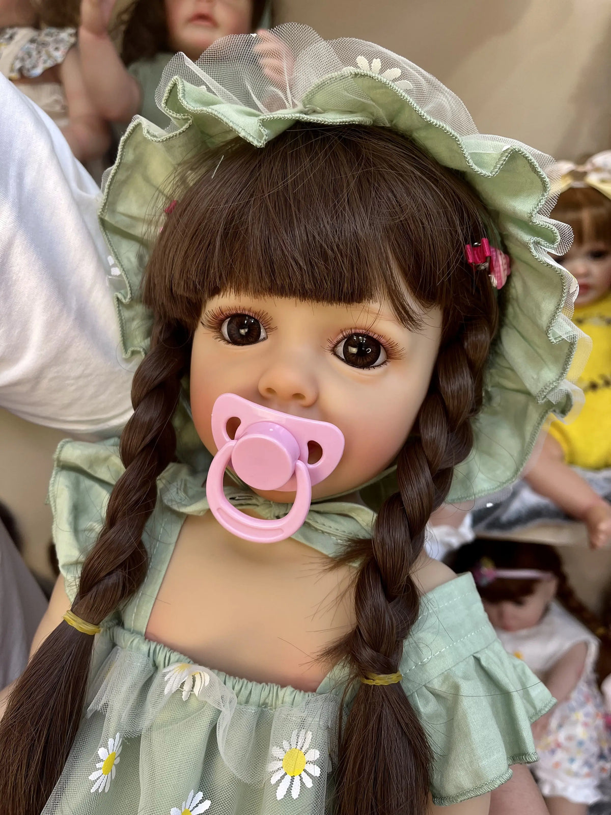 A realistic silicone vinyl toddler doll named Betty with dark hair styled in braids wearing a light green dress.