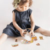 A young girl is interacting with a wooden animal threading and stacking toy set on a white surface.