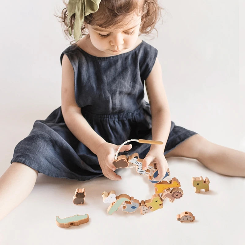 A young girl is interacting with a wooden animal threading and stacking toy set on a white surface.