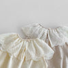 A close-up of a cream colored baby girl sleeveless jumpsuit featuring delicate white lace collars and puff sleeves.