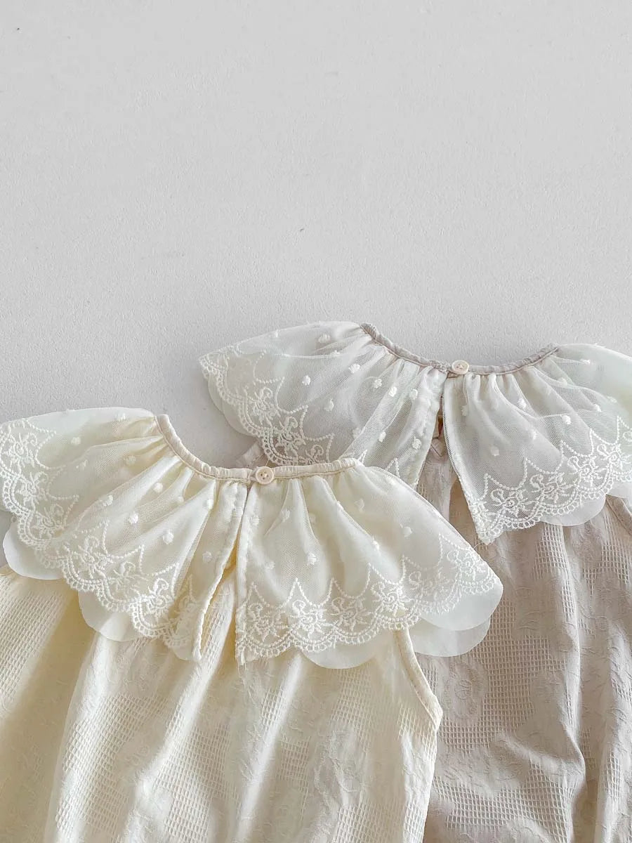 A close-up of a cream colored baby girl sleeveless jumpsuit featuring delicate white lace collars and puff sleeves.