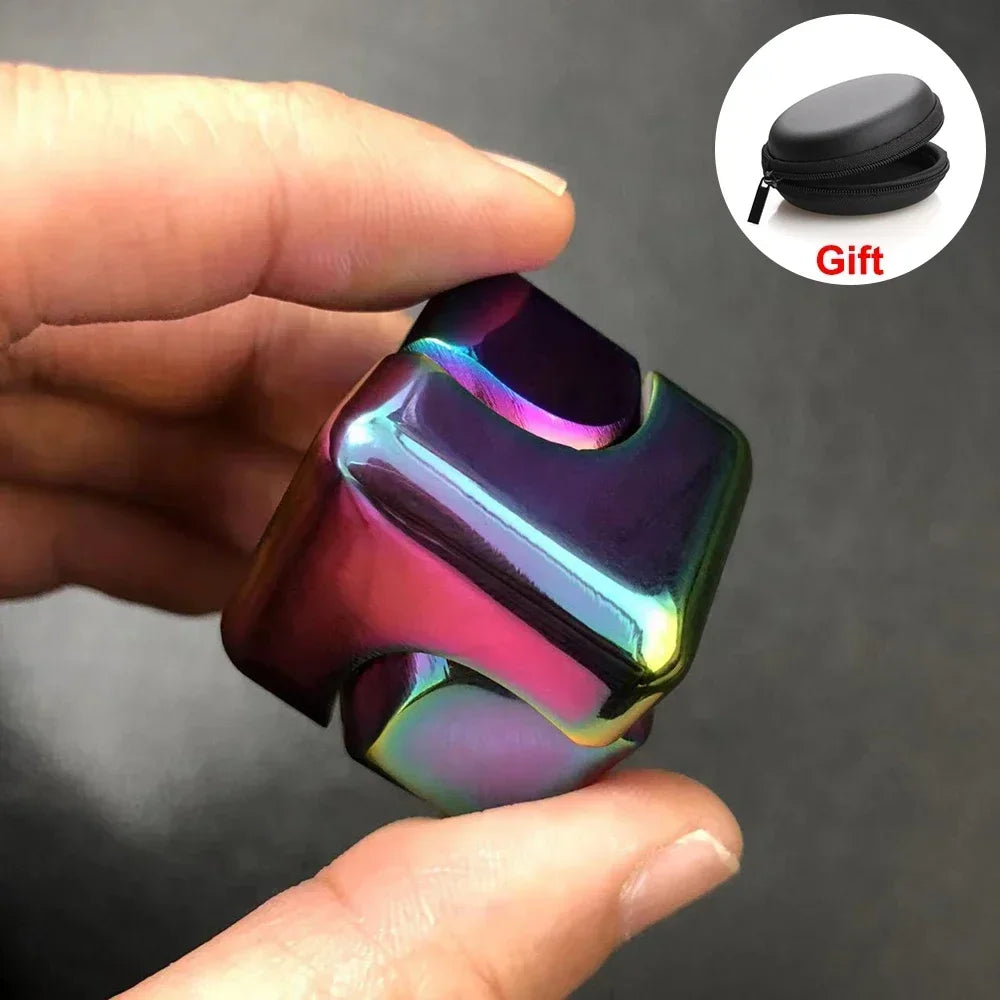 Une main tient un cube jouet à faire tourner, irisé violet et rose, avec un sac cadeau noir à proximité.