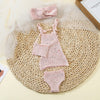 A pink knitted doll outfit set for a baby doll featuring a top, shorts, and a matching bow.