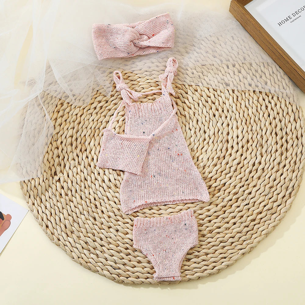 A pink knitted doll outfit set for a baby doll featuring a top, shorts, and a matching bow.