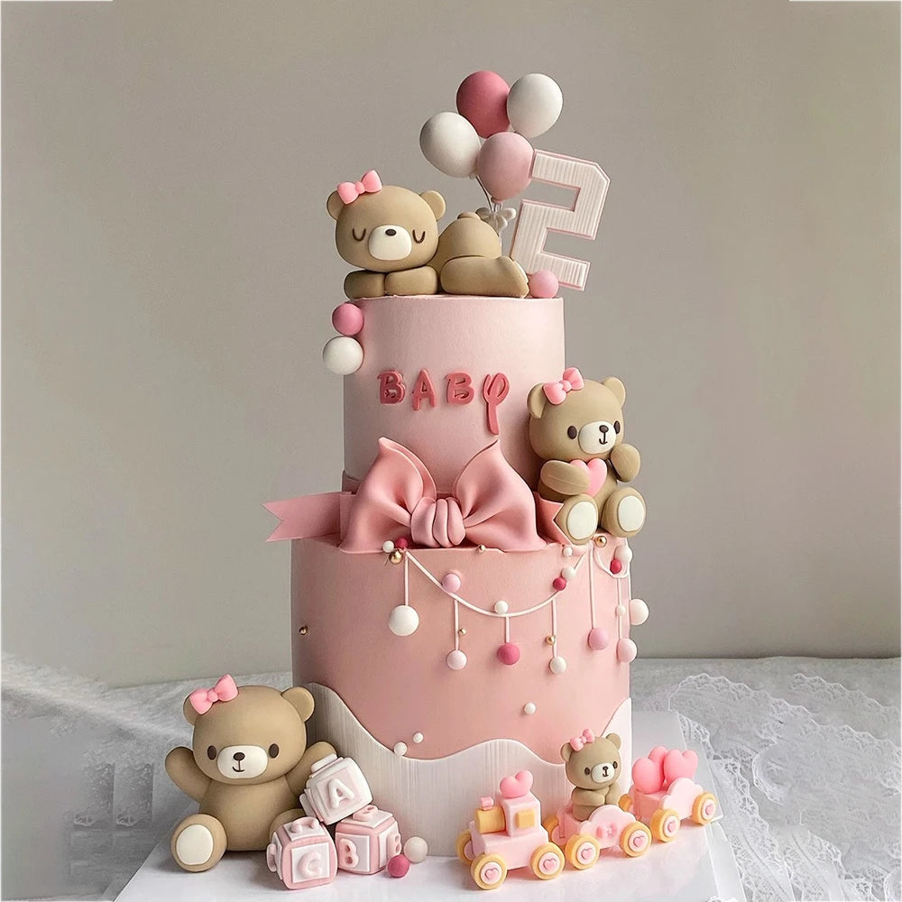 A tiered pink cake decorated with teddy bear figures and pink accents for a birthday or baby shower.