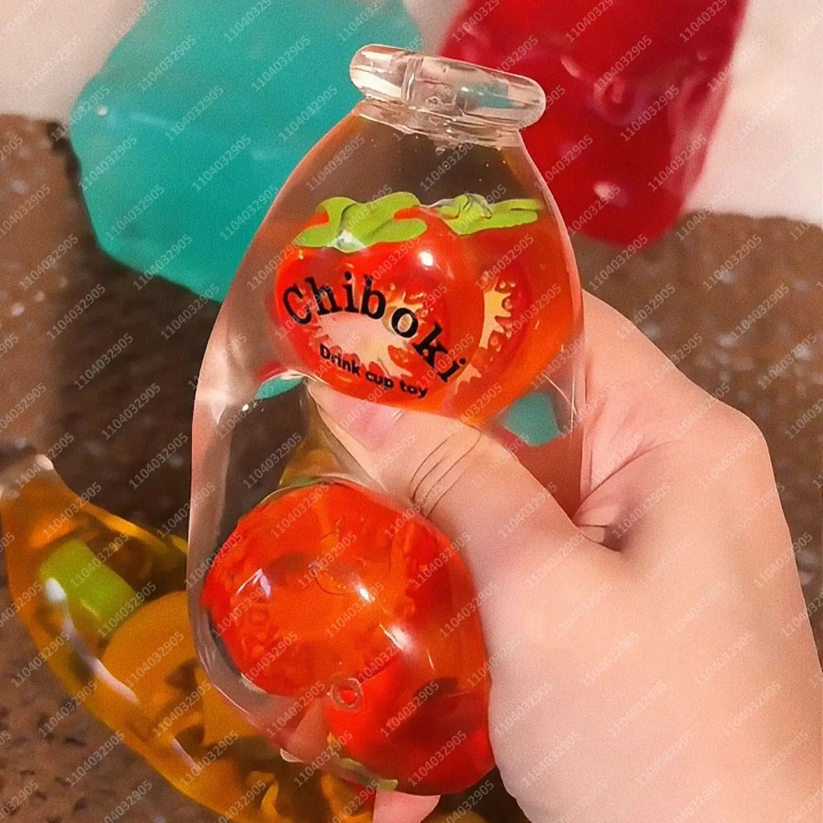 A hand holds a clear bottle shaped like a strawberry with a green top, part of a fruit bottle stress ball set.
