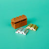 An open wooden treasure chest containing gold and silver building blocks on a teal background.