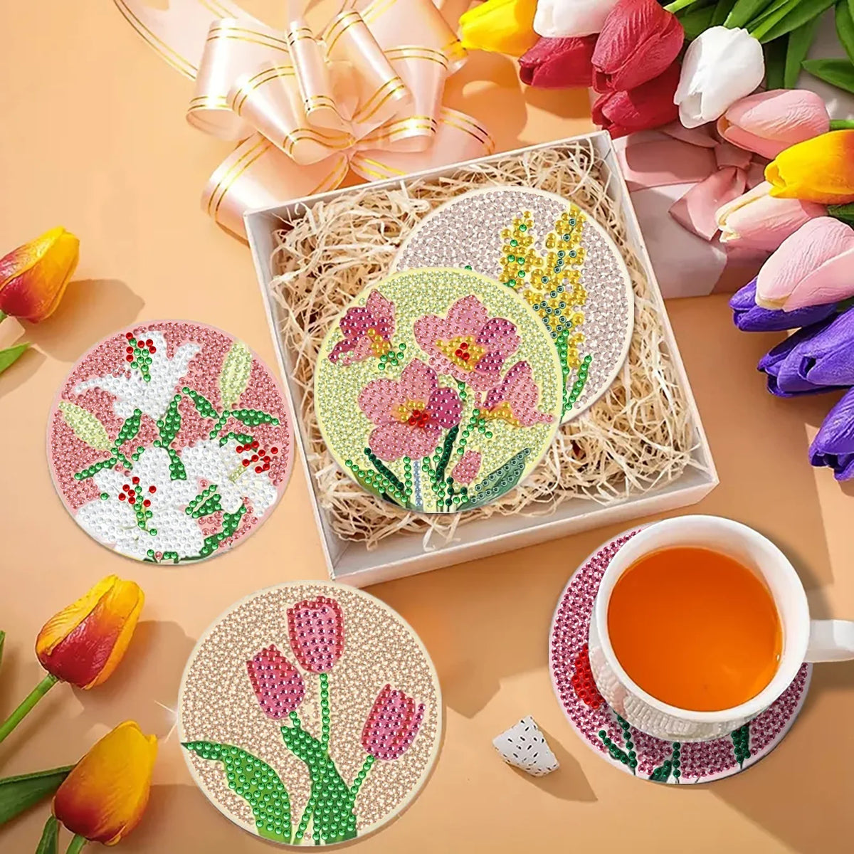 A set of floral diamond painting coasters featuring pink and yellow flowers displayed with a metal holder and tea.