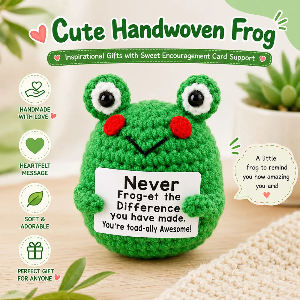 A handmade crochet frog doll in green with red eyes and a motivational card on a wooden surface.