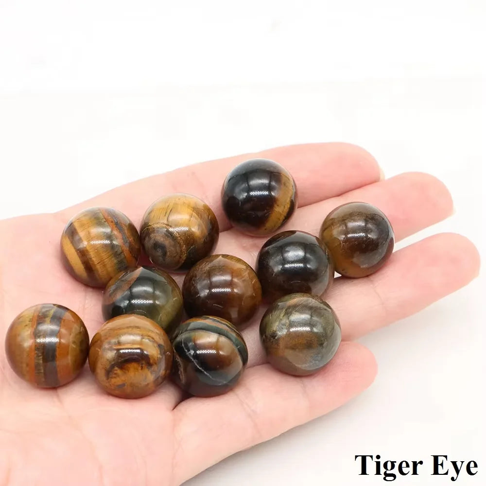 A hand holds several polished Tiger Eye crystal spheres of varying sizes and shades.