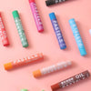 A collection of oil pastels in various colors including pink, green, blue, and orange lying on a light pink surface.
