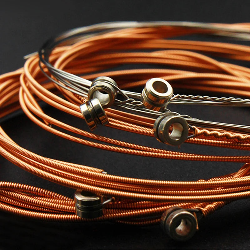 A coil of rust-resistant acoustic guitar strings with a string changer tool laid out on a dark surface.