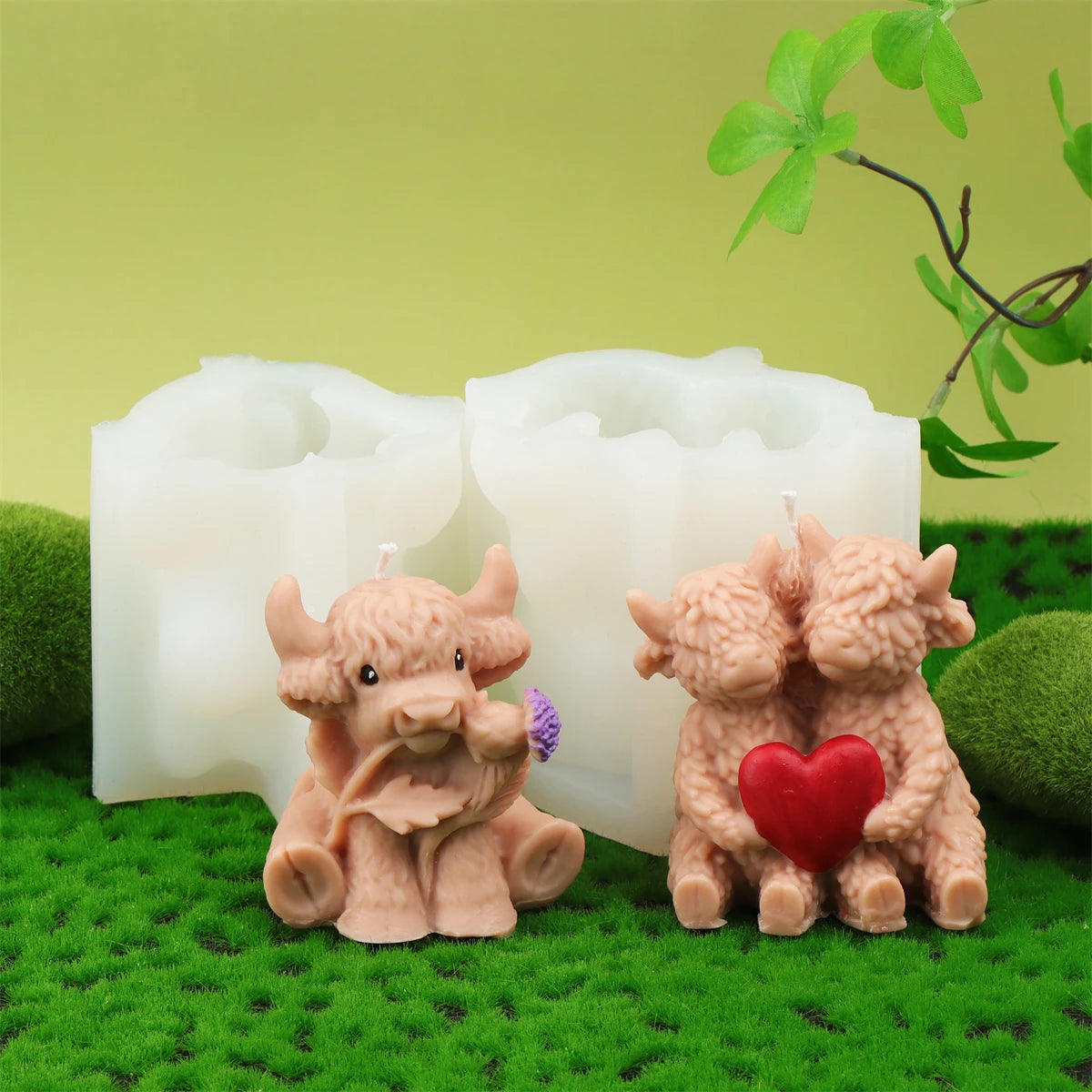 A set of four silicone candle molds shaped like Highland cows, including one with a red heart detail, resting on green moss.