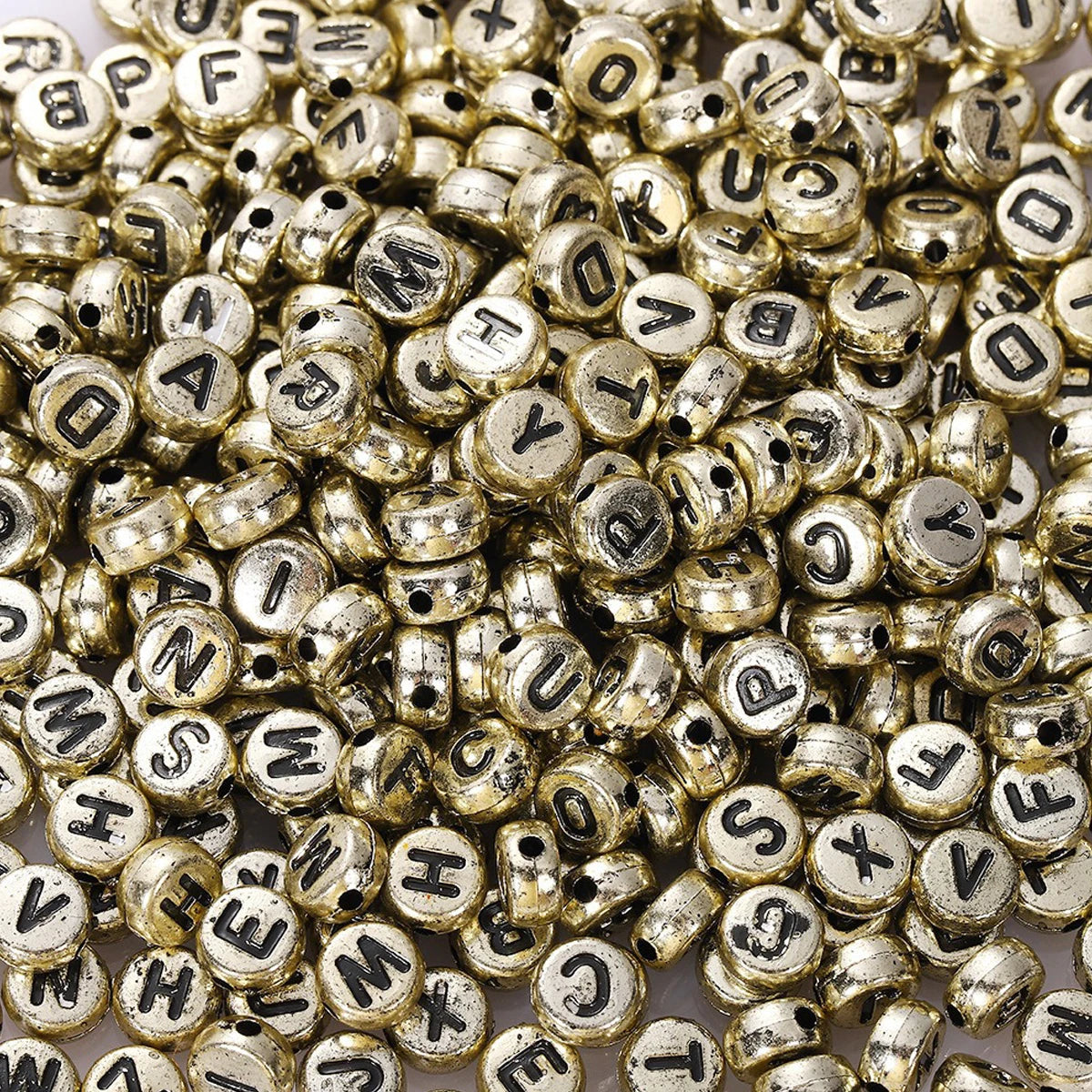 A close-up view of many small, round, gold-colored acrylic alphabet beads for jewelry making.