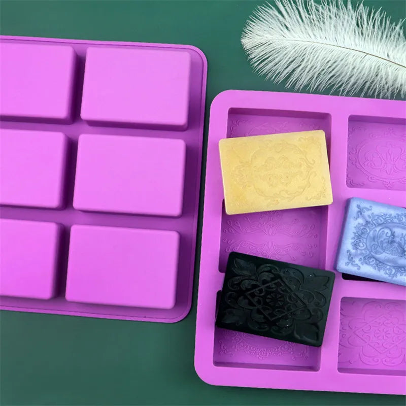 A pink silicone soap mold tray with six square cavities, featuring yellow and blue floral pattern soaps.