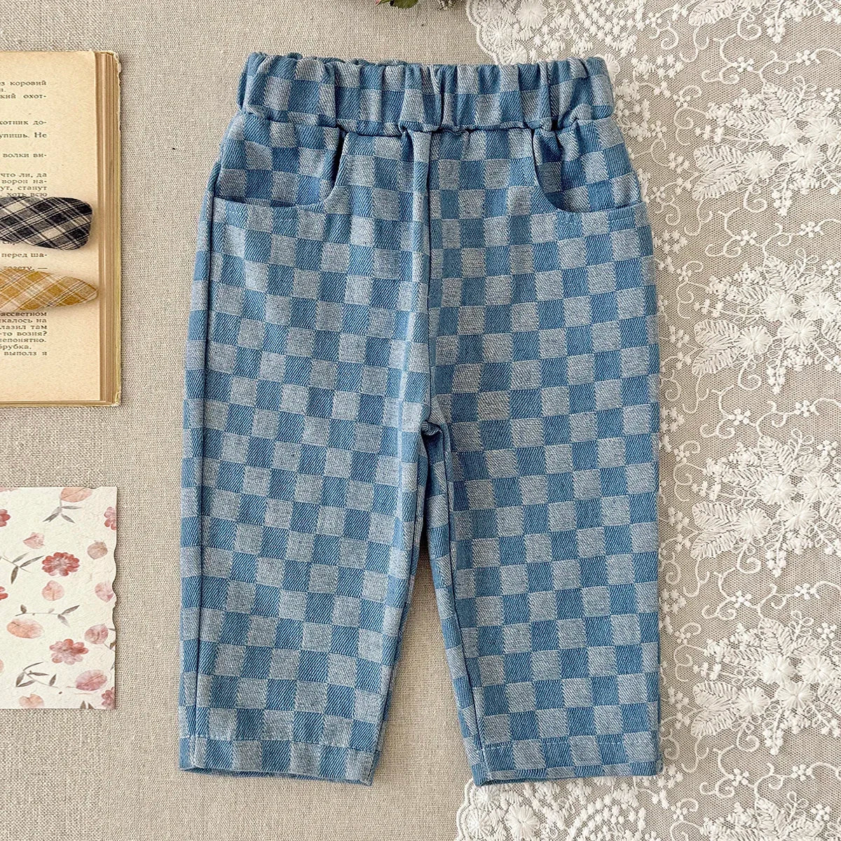 Blue and blue plaid corduroy pants with elastic waist for toddlers lying on a light fabric.