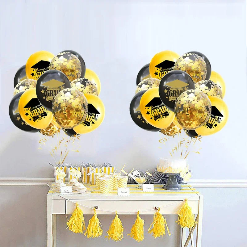 A set of black and gold confetti balloons decorated with graduation text, displayed on a white table.