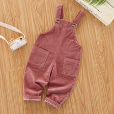 A pair of dusty rose baby cotton overalls with adjustable straps lying on a wooden surface.