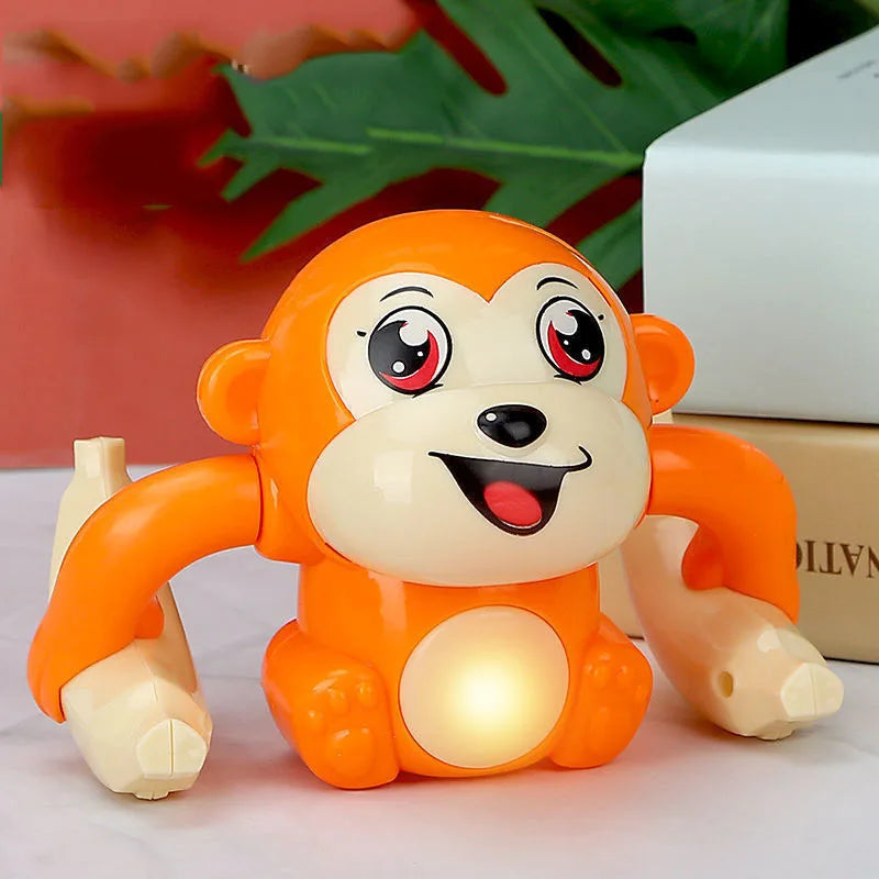 Jouet singe électrique orange et roulant avec de grands yeux et un sourire, assis sur une surface blanche.